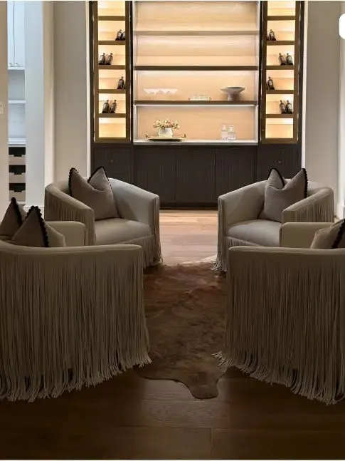 Luxe Design Group post: four fringed armchairs around a cowhide rug in front of lit built-in shelving.